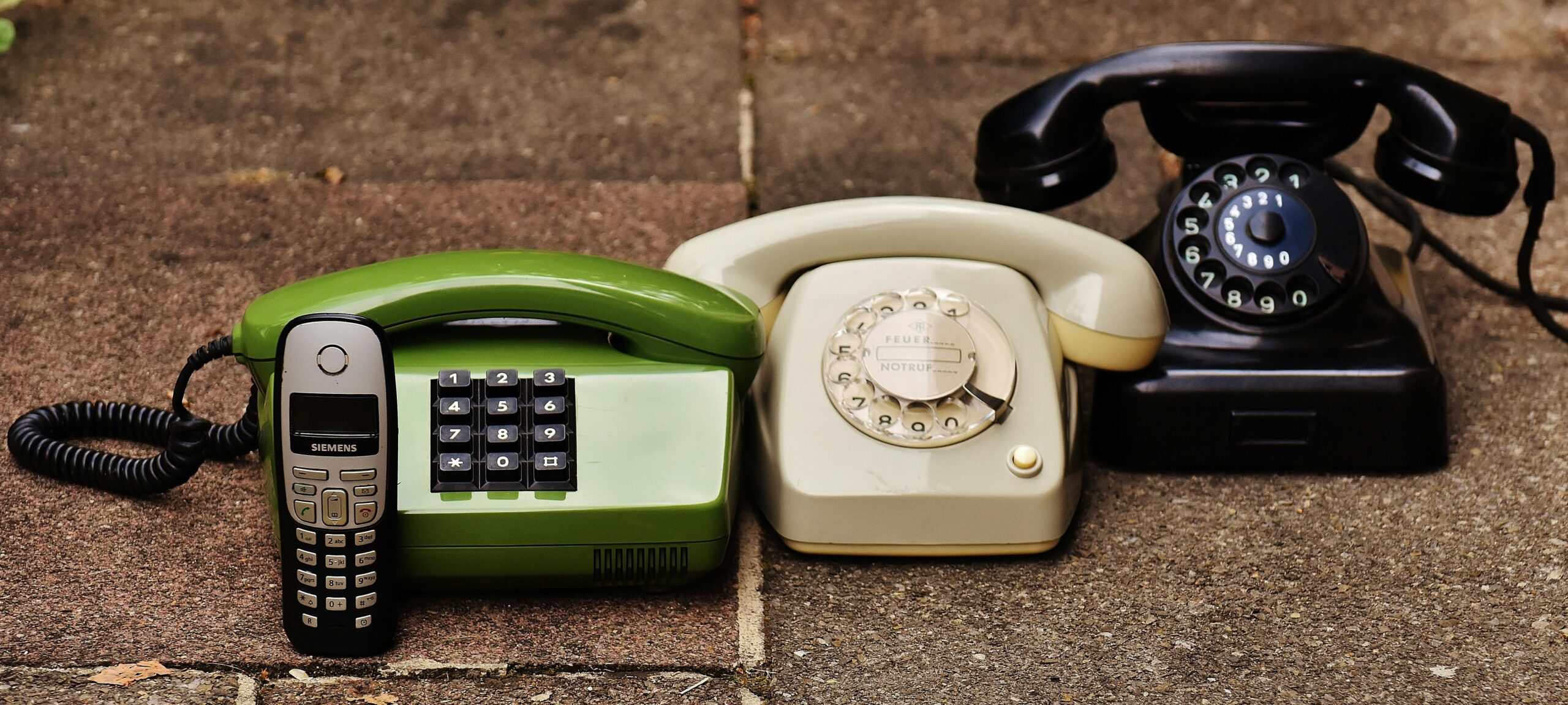 A variety of antique, vintage, and modern telephones displayed on pavement.